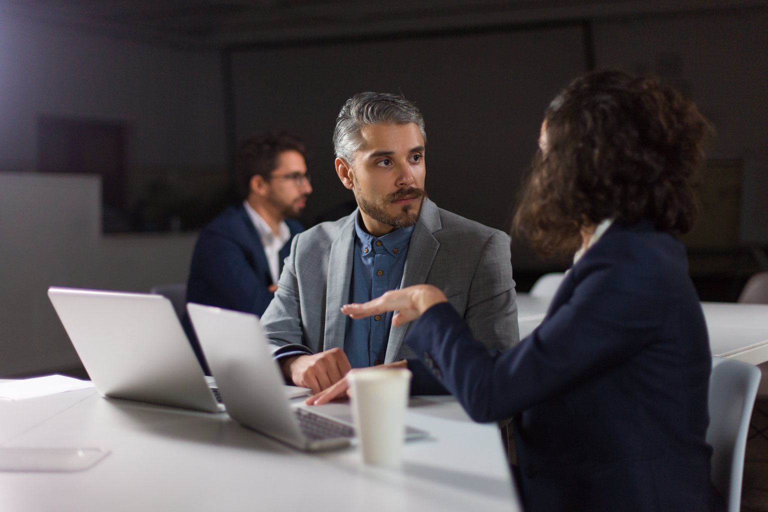 Reunião de trabalho em sala com luz baixa, executivos debatendo ao redor da mesa
